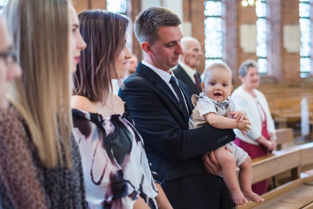 Rodzina podczas chrztu w kościele – ojciec trzymający uśmiechnięte dziecko, eleganckie stroje, uroczystość chrztu świętego