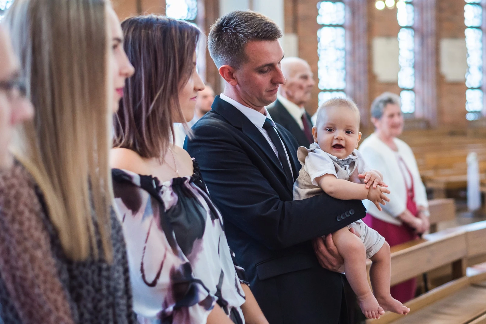 Rodzina podczas chrztu w kościele – ojciec trzymający uśmiechnięte dziecko, eleganckie stroje, uroczystość chrztu świętego