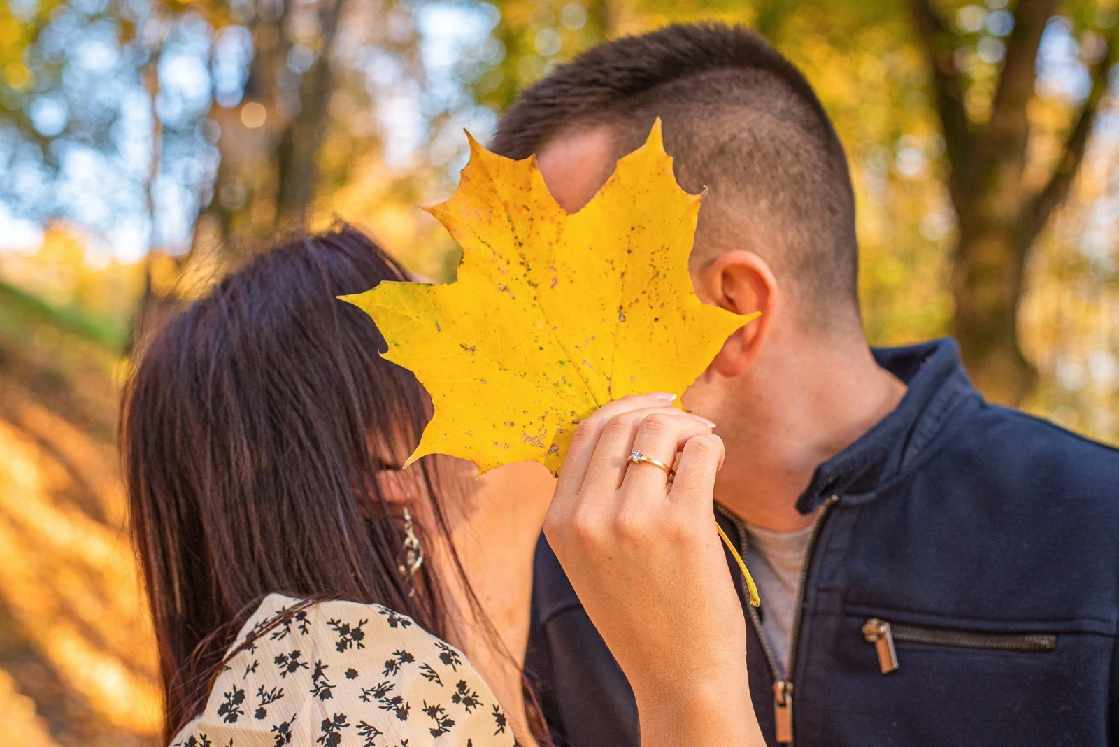Jesienna sesja narzeczeńska – para zakochanych całująca się za liściem klonu, zaręczynowy pierścionek, fotografia ślubna plenerowa